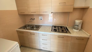 Een kleine keuken met een spoelbak, fornuis en kastjes.