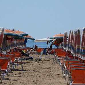 A beach with rows of orange beach chairs and colorful umbrellas.