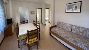 A dining area with a table and chairs, a sofa, a TV, and a ceiling light. - Rose in Bibione With 3 Bedrooms and 1 Bathrooms (San Michele al Tagliamento)