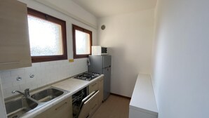 A compact kitchen with a gas stove, two sinks, a dishwasher, and a refrigerator. - Rose in Bibione With 3 Bedrooms and 1 Bathrooms (San Michele al Tagliamento)