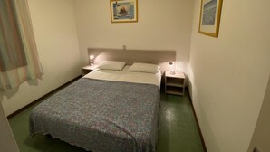 A hotel room with a bed, two bedside tables with lamps, a window with a curtain, and two framed pictures on the walls. - Rose in Bibione With 3 Bedrooms and 1 Bathrooms (San Michele al Tagliamento)