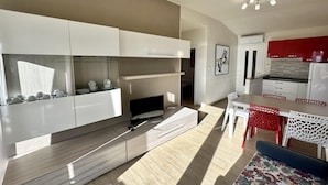 A modern kitchen with white cabinetry, a built-in oven, and a dining area with a table and chairs. - Villa Beba 1P in Bibione (San Michele al Tagliamento)