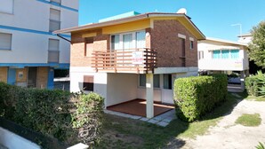 A two-story residential building with a balcony, a small front yard, and a neighboring taller building. - Villa Beba 1P in Bibione (San Michele al Tagliamento)