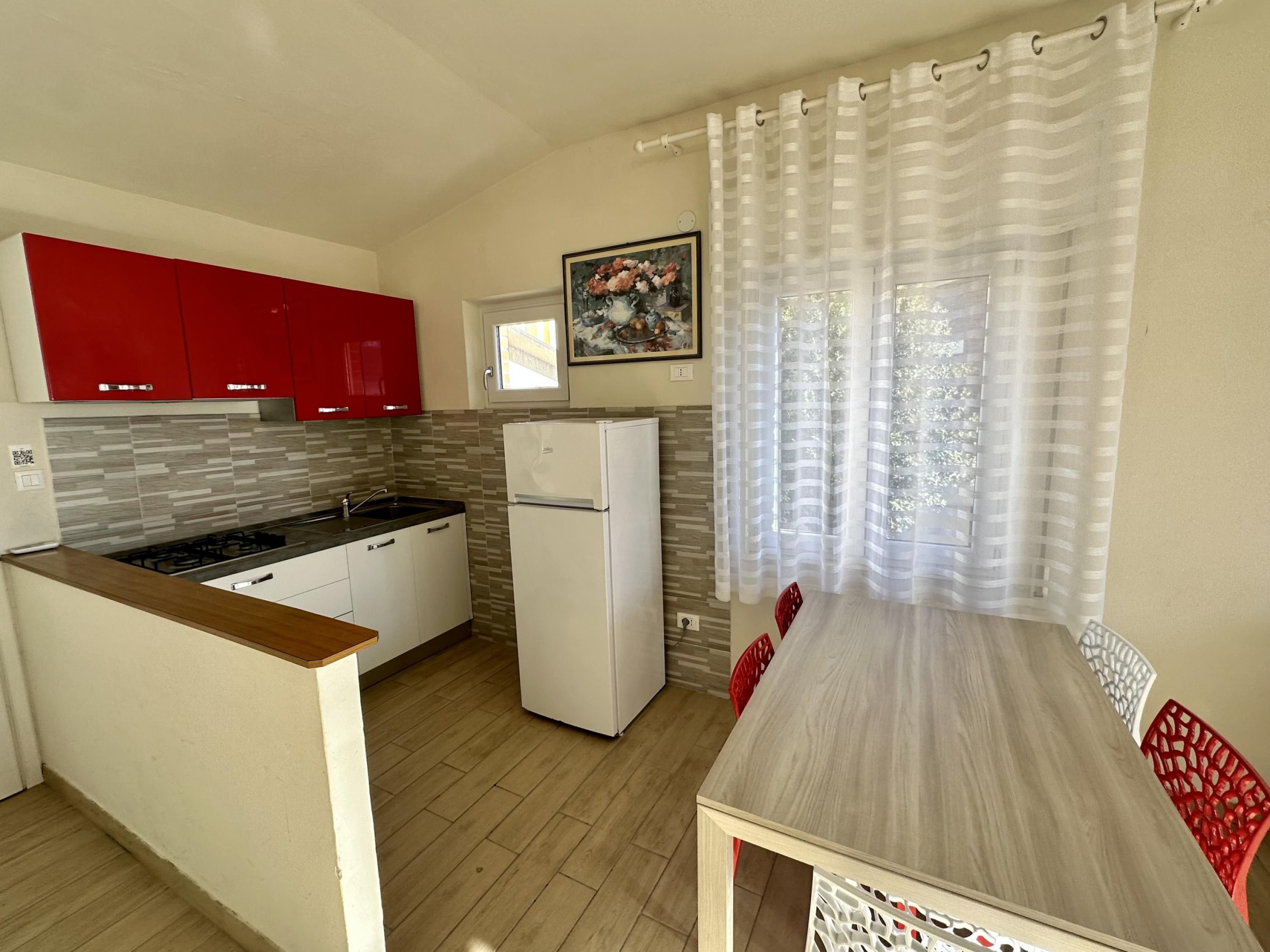 Une cuisine de taille réduite, équipée d’un réfrigérateur, d’une cuisinière et de meubles de rangement rouges.