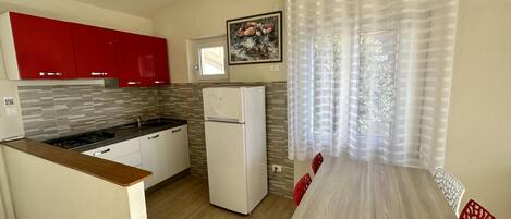 Une cuisine de taille réduite, équipée d’un réfrigérateur, d’une cuisinière et de meubles de rangement rouges.