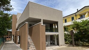 A modern building with a flat roof, a staircase leading to an upper level, and a small outdoor seating area with chairs. - Diana 5 in Bibione With 1 Bedrooms and 1 Bathrooms (San Michele al Tagliamento)