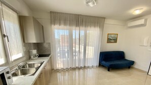 A modern kitchen with stainless steel appliances, a blue sofa, and a large window with sheer curtains. - Diana 5 in Bibione With 1 Bedrooms and 1 Bathrooms (San Michele al Tagliamento)