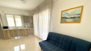A spacious living area with a blue sofa, a kitchen with wooden cabinets, and a painting on the wall. - Diana 5 in Bibione With 1 Bedrooms and 1 Bathrooms (San Michele al Tagliamento)