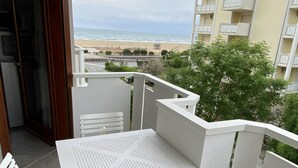 Un balcon avec une table et des chaises blanches, une vue sur la plage et un immeuble doté de balcons.