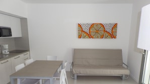 Een moderne keuken met witte kastjes, een magnetron en een eethoek met een tafel en stoelen.