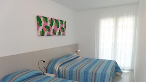 Een slaapkamer met twee bedden, wanddecoratie in roze en groen, en een raam met dunne gordijnen.