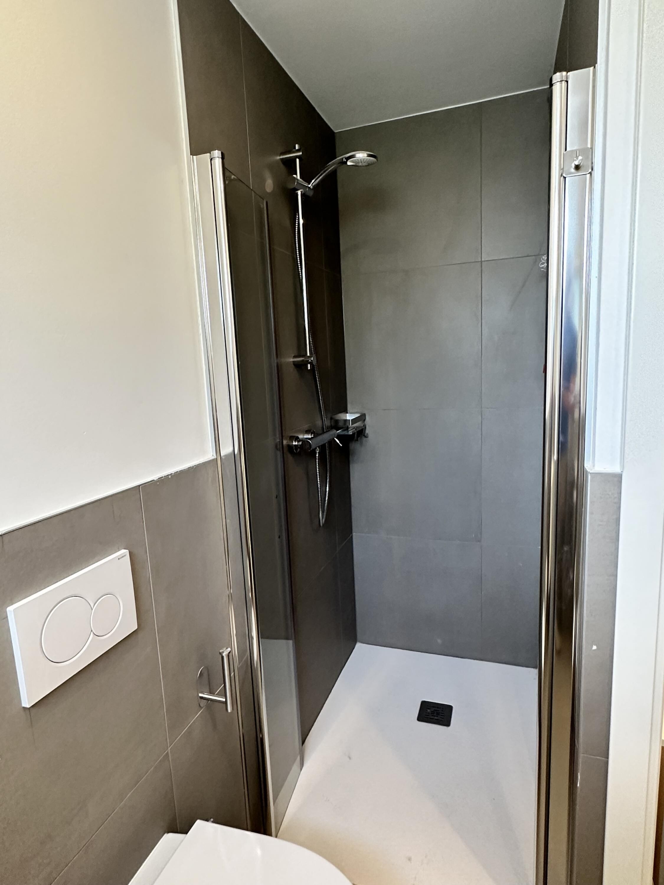 Um chuveiro moderno com porta de vidro, um chuveiro manual e painel de controle na parede.
