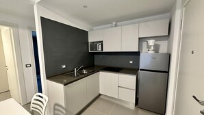 A modern kitchen with white cabinets, a black countertop, a stainless steel refrigerator, and a built-in microwave. - Skipper C6 in Bibione (San Michele al Tagliamento)