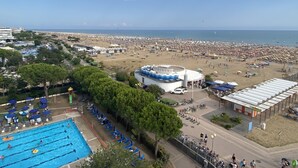 A beach resort with a swimming pool, beach umbrellas, and a large building with a blue and white facade. - Skipper C6 in Bibione (San Michele al Tagliamento)