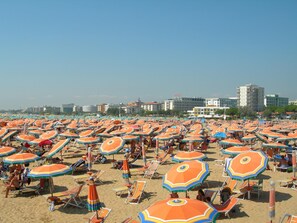 A beach with numerous colorful umbrellas and sun loungers, with buildings in the background.