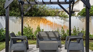 Une terrasse couverte avec un canapé en osier et deux fauteuils.