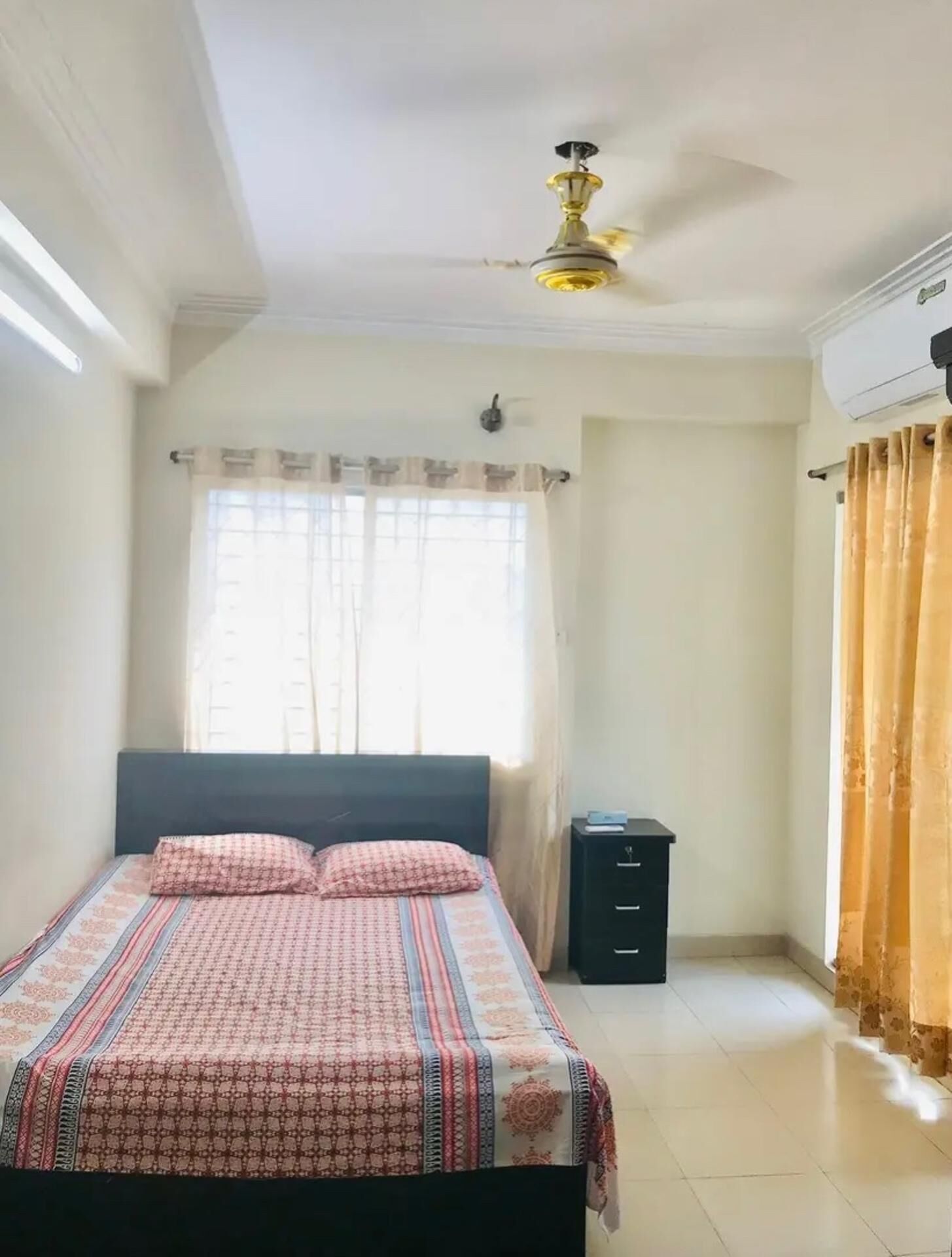 A bedroom with a bed, a nightstand, a ceiling fan, and a window with curtains.