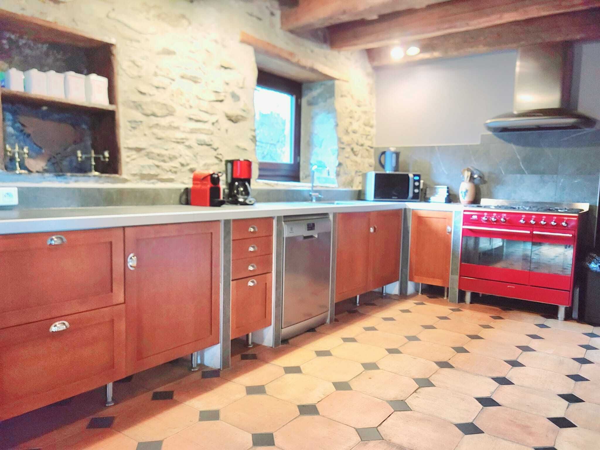 Una cocina con armarios de madera, una estufa roja, lavavajillas y una pared de piedra.