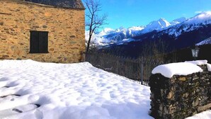 A stone building with a snow-covered roof and a mountain backdrop.