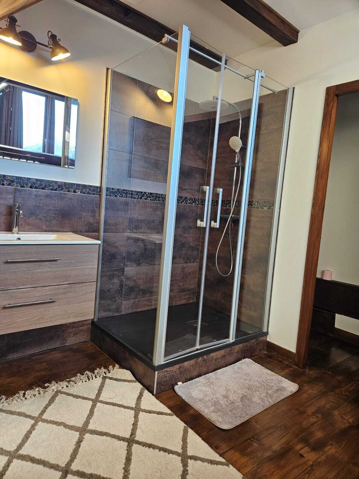 Ein modernes Badezimmer mit einer gläsernen Dusche, einem Holzkosmetikschrank und einem großen Spiegel.