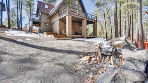 A two-story house with a balcony, surrounded by trees and a rocky landscape.