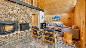 A cozy interior with a stone fireplace, wooden furniture, and a view of the outdoors.