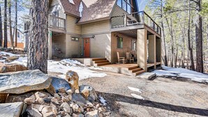 A modern cabin with a two-story structure, large windows, and a covered porch with outdoor seating.