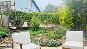A patio with two white cushioned chairs and a wooden table. - Charming Cottage Retreat (Oakland)