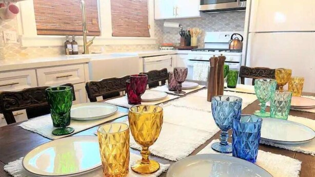 A dining area with a wooden table set for four, featuring colorful glassware and plates. - Charming Cottage Retreat (Oakland)