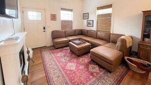 A living room with a sectional sofa, a flat-screen TV mounted on the wall, a ceiling fan, and a patterned rug. - Charming Cottage Retreat (Oakland)