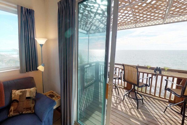 A balcony with a view of the sea, a sofa with a cushion, a lamp, and a table with chairs. - Beachfront 2BR Paradise w/ Sweeping Gulf Views; Walking to Shops & Restaurants! (Bradenton Beach)