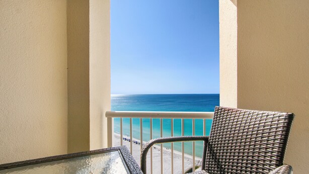 A balcony with a view of the ocean, a wicker chair, and a glass table. - Oceanfront ex large balcony, Amazing panoramic views of Gulf from 16th floor (Panama City Beach)
