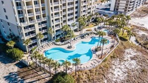A multi-story hotel with a central swimming pool surrounded by palm trees and lounge chairs. - Oceanfront ex large balcony, Amazing panoramic views of Gulf from 16th floor (Panama City Beach)