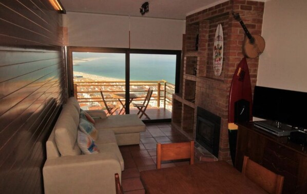 A living room with a large window, a fireplace, and a view of the beach.