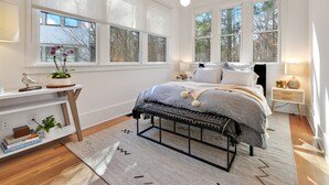 A bedroom with a bed, bedside tables, a desk, and large windows.