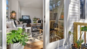 A modern living room with a sofa, coffee table, and TV. There is a sliding glass door leading to a balcony with plants.