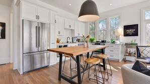 A modern kitchen with white cabinetry, stainless steel appliances, a wooden island with stools, and a pendant light.