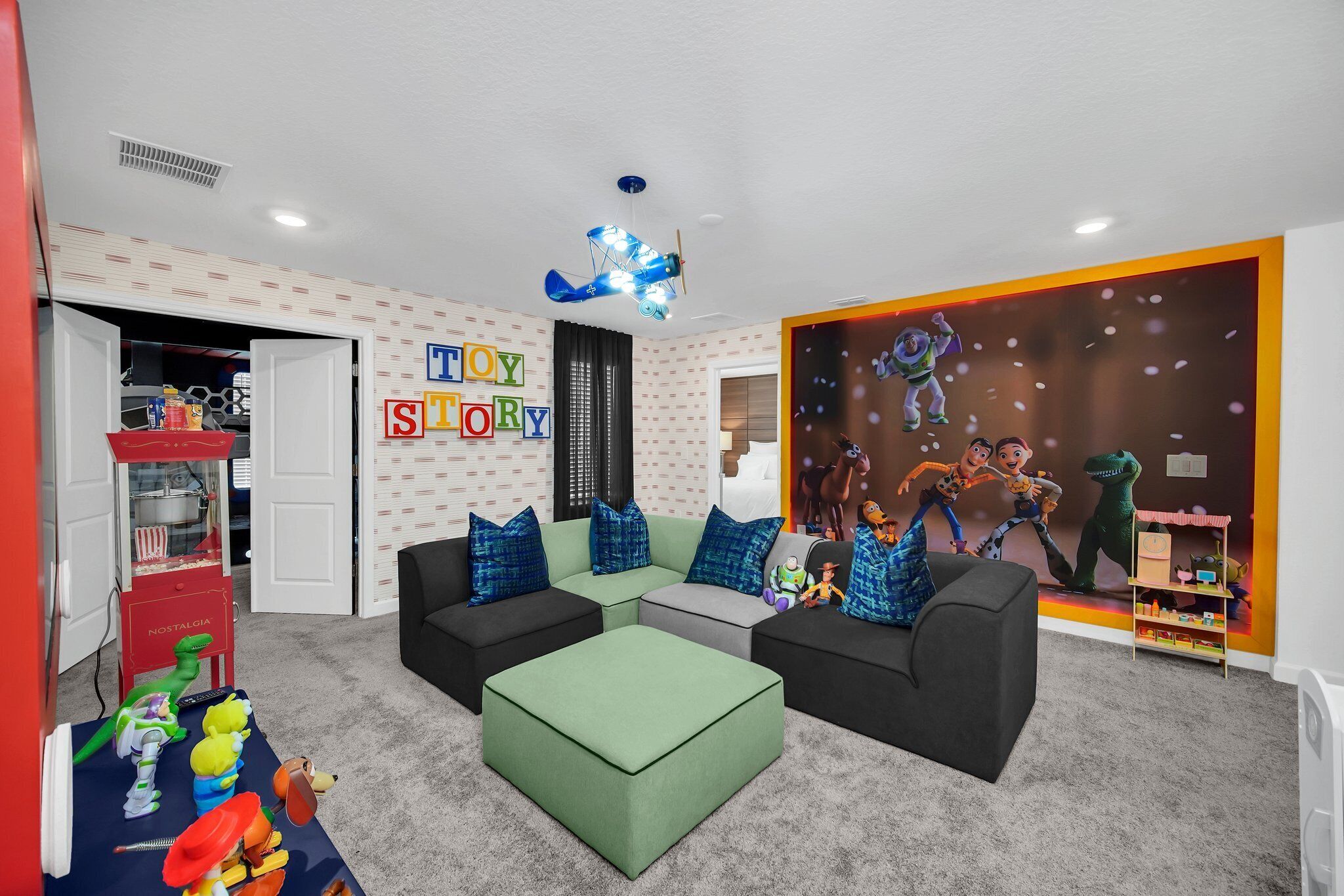 Une salle de jeux pour enfants avec un canapé vert, un distributeur de pop-corn rouge et une fresque murale représentant les personnages de Toy Story.