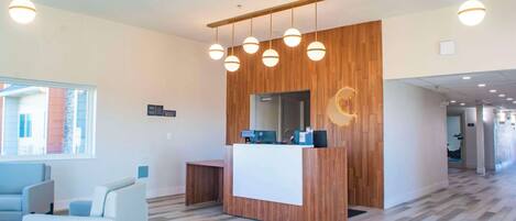 Un área de recepción moderna con un mostrador de madera, múltiples lámparas colgantes y un espacio de estar con un sofá y sillones.