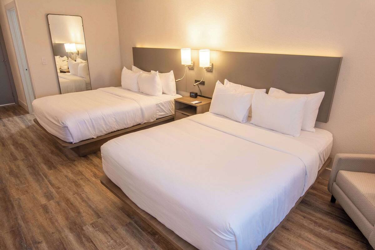 A hotel room with two single beds, a nightstand with a lamp, a mirror, and a chair.