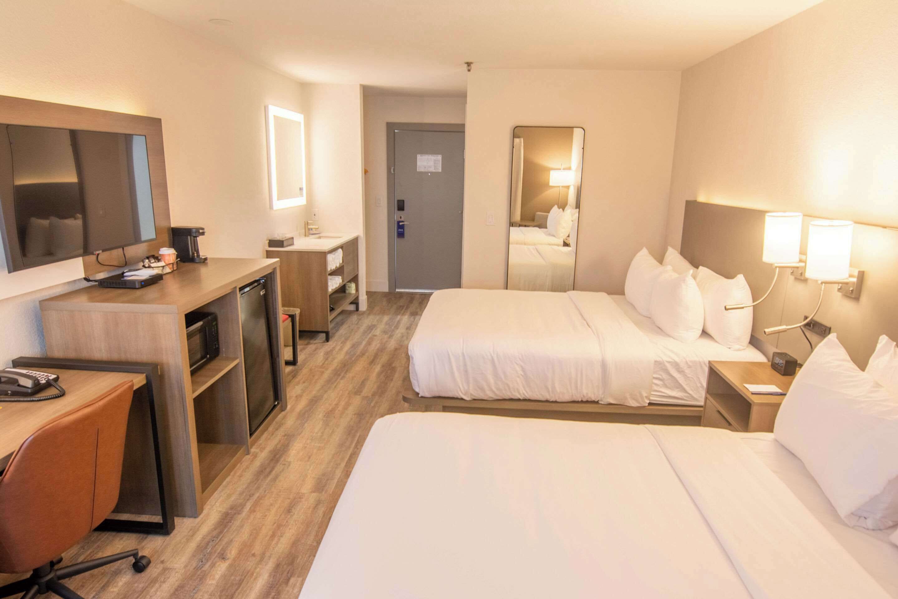 A hotel room with two beds, a desk with a computer, a TV, and a minibar.