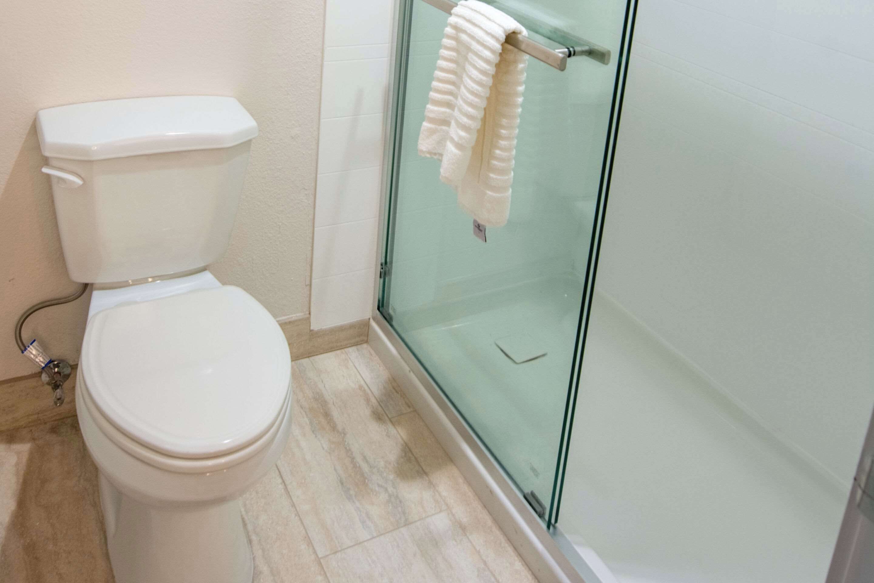 A bathroom with a toilet, a glass shower enclosure, and a towel hanging on the shower door handle.