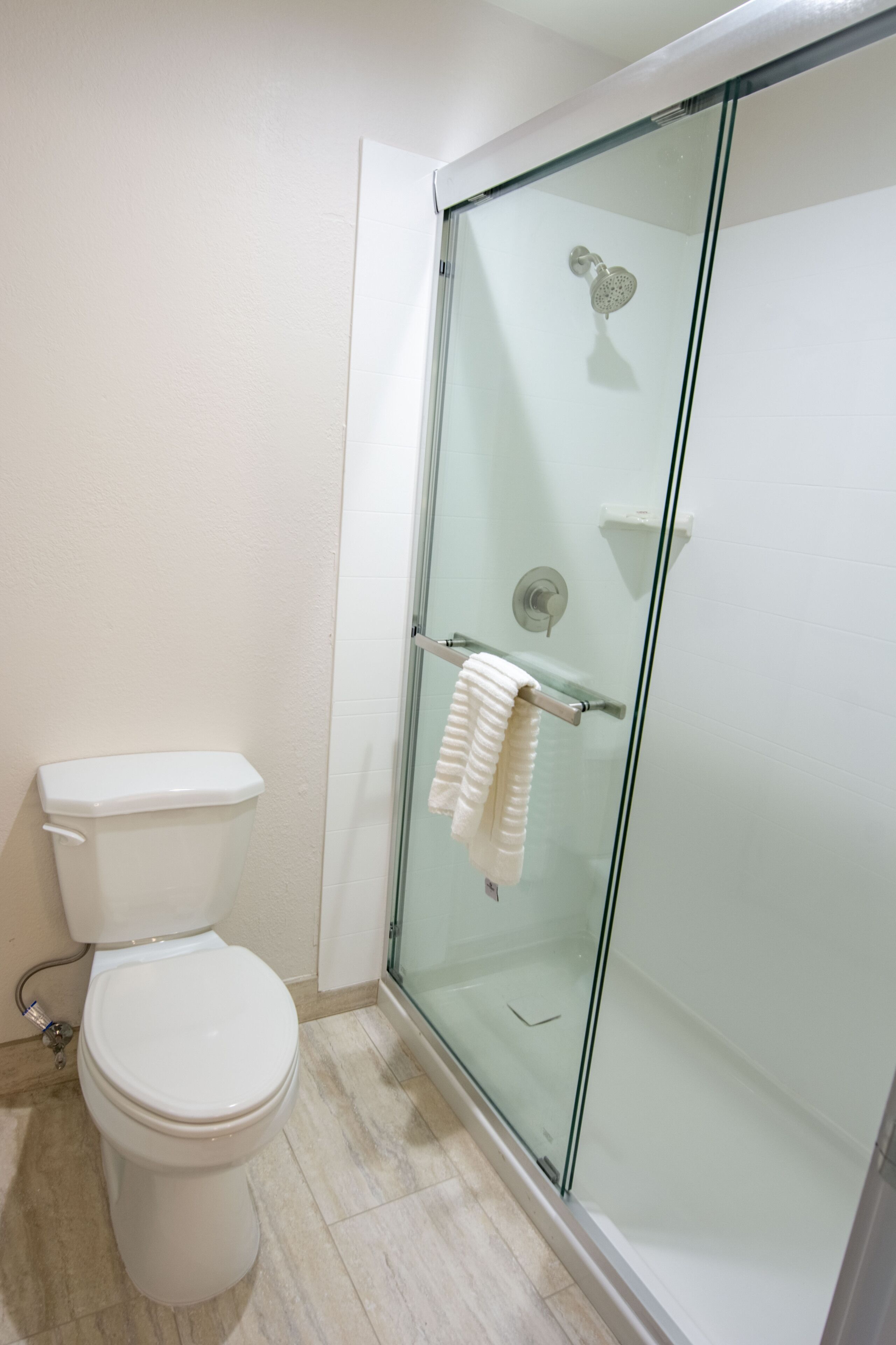 A bathroom with a glass-enclosed shower, a white toilet, and a towel rack with a white towel.