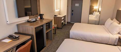 Una habitación de hotel con escritorio, dos camas, televisión, espejo y baño.