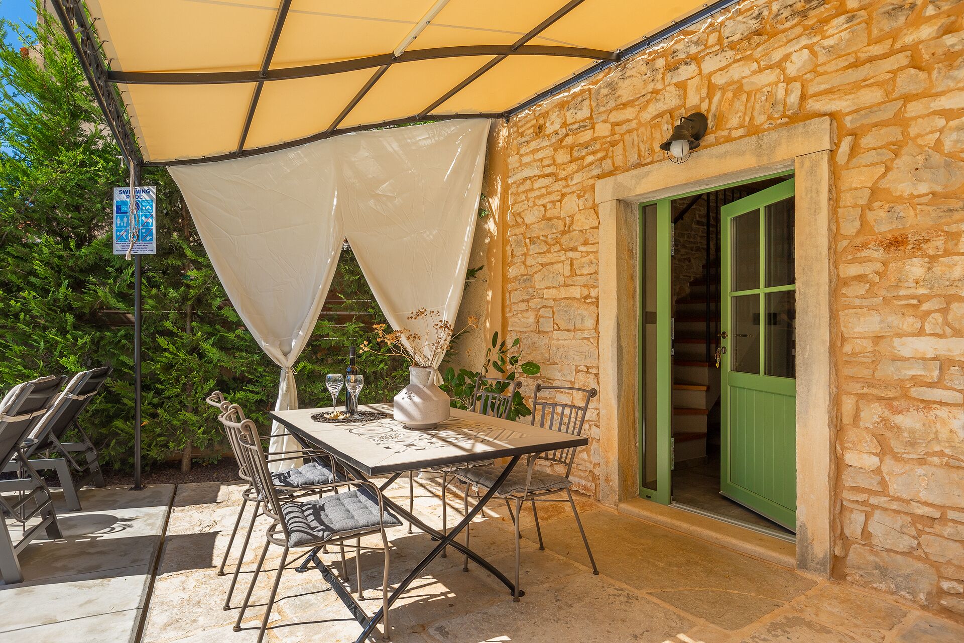 Um pátio externo com mesa, cadeiras, parede de pedra e porta verde.