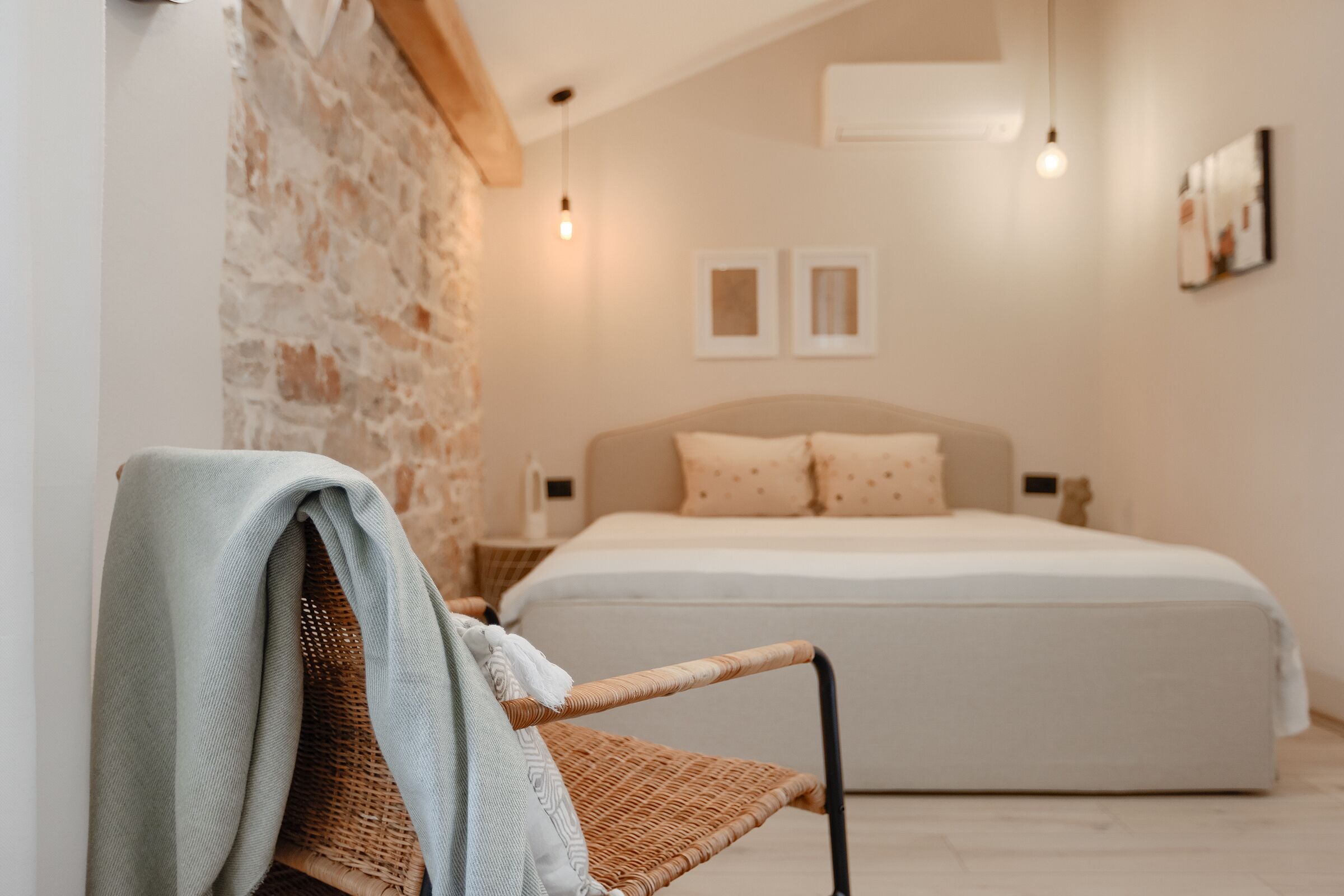 Une chambre avec un lit, une table de chevet, un fauteuil en osier et un mur en briques apparentes.