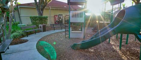 A playground with a slide, benches, and a playhouse.