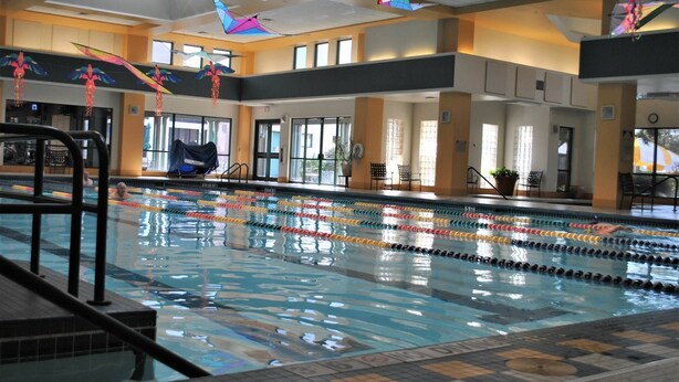 Una piscina interior con demarcaciones claras para carriles, una silla de salvavidas y una zona de estar cubierta con sillas y una planta.