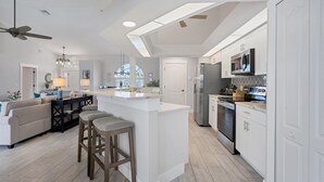Eine moderne Küche mit Kochinsel, Essbereich inklusive Sofa und Barhocker sowie Deckenventilator.