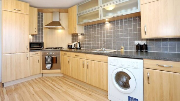 Een moderne keuken met houten kastjes, een magnetron, fornuis en een wasmachine.